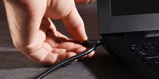 A male hand plugging laptop battery cable Quando carregar a bateria do meu laptop